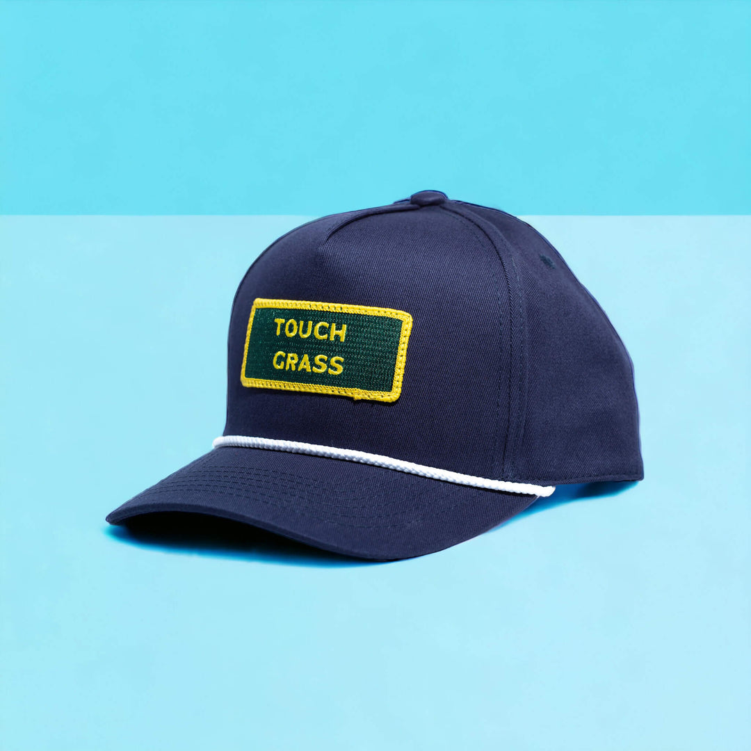 A blue captains hat with a gold and green patch that says "Touch Grass' on a baby blue background.