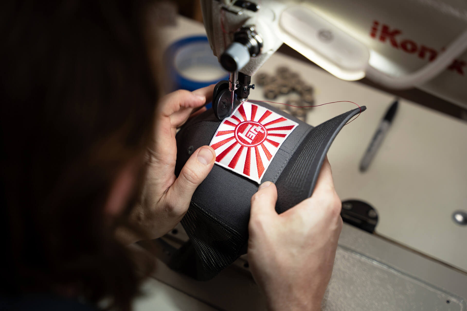 Hand Stitching a red and white Rising Sun TEQ patch on a dark grey trucker hat